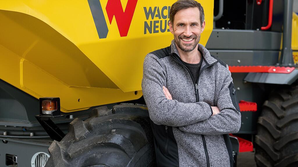 Un client Wacker Neuson souriant et les bras croisés devant un dumper sur pneus de Wacker Neuson.