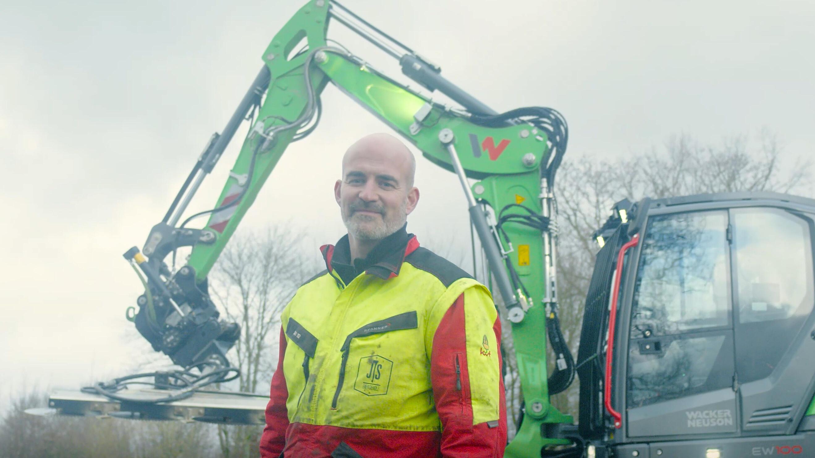 Un opérateur se tient devant une pelle sur pneus Wacker Neuson EW100 équipée d'un tiltrotator.