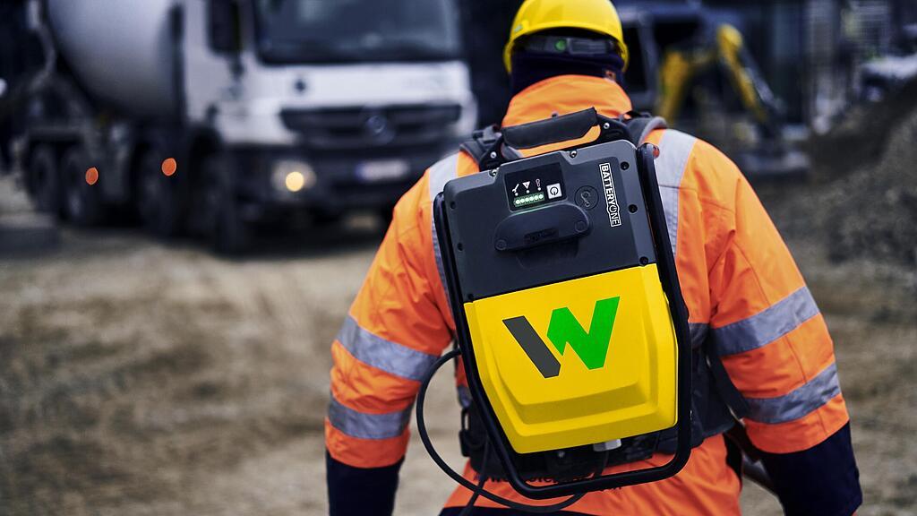 Un ouvrier porte le sac à dos pour convertisseur de batterie ACBe de Wacker Neuson sur un chantier.